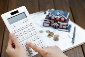 Homeowner using a calculator to estimate ADU construction costs with house plans and coins
