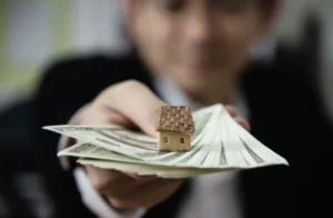 Property owner holding cash and a small model house representing monthly rental payments